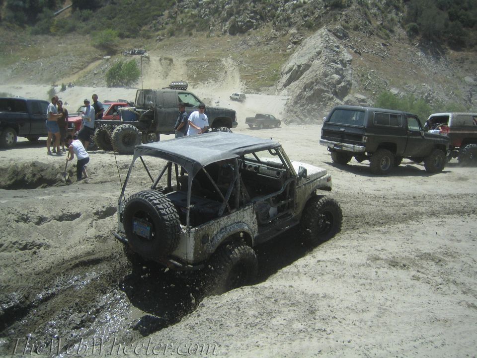 White off-road vehicle stuck in mud, with other vehicles and people in the background