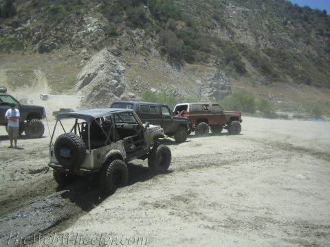 1987 Suzuki Samurai - A group of modified off-road vehicles are parked on a dirt track, ready for adventure.