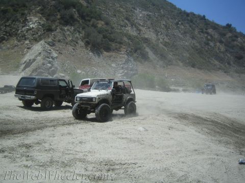1987 Suzuki Samurai - Multiple off-road vehicles are seen in a dusty, mountainous terrain.