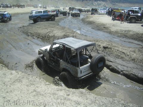 1987 Suzuki Samurai - Several vehicles are seen off-roading on a muddy beach, with one Suzuki Samurai in the foreground struggling through the mire.