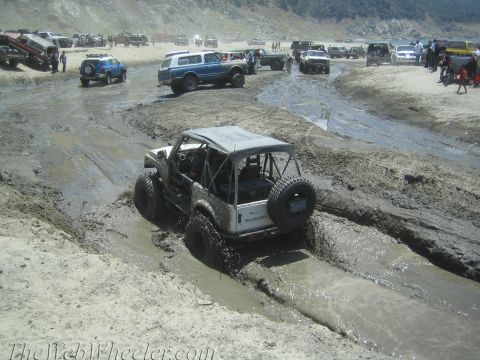 1987 Suzuki Samurai - A Suzuki Samurai tackles a challenging muddy course with other off-road vehicles in the background.