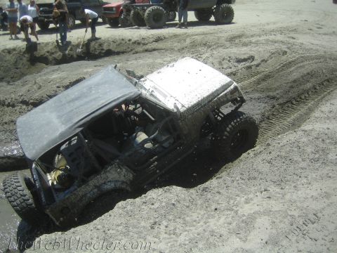 1987 Suzuki Samurai - Off-road vehicle stuck in mud pit during an event, with spectators and other trucks nearby.