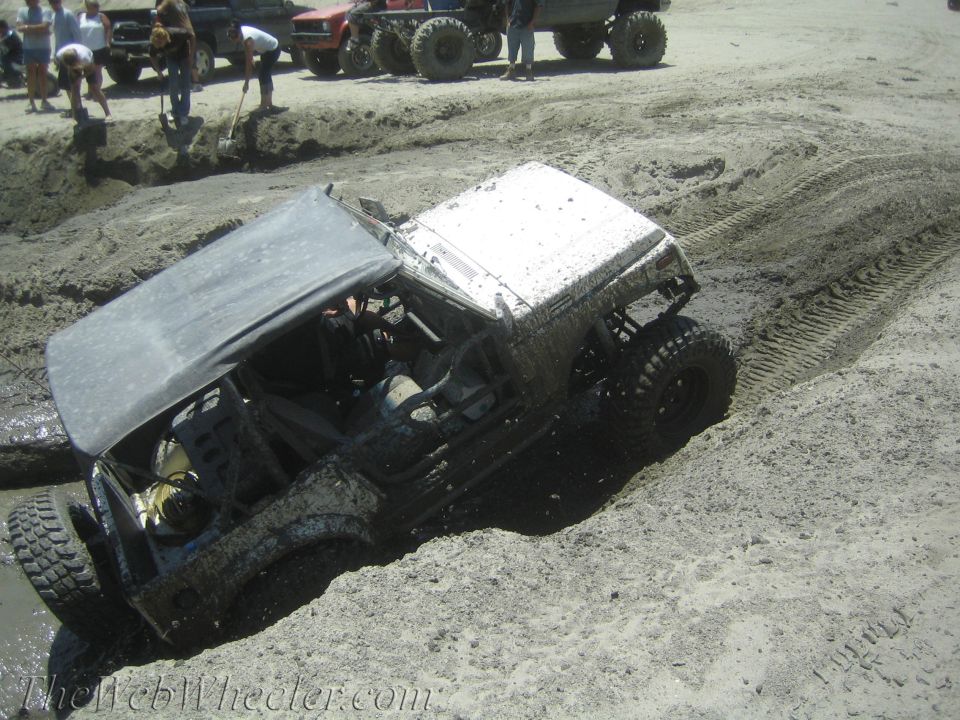 1987 Suzuki Samurai partially submerged in mud, soft top up, with other off-road vehicles and people in the background