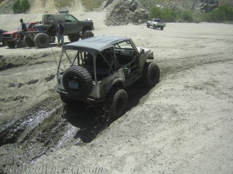 1987 Suzuki Samurai - Several off-road vehicles navigate a muddy terrain under a bright sky.