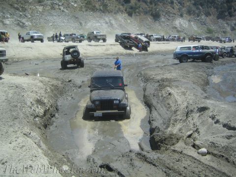 1987 Suzuki Samurai - Multiple off-road vehicles are seen navigating a challenging muddy terrain during an outdoor event.