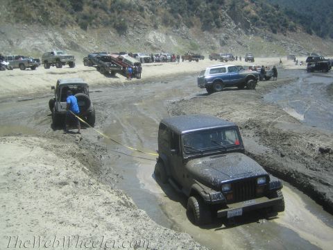1987 Suzuki Samurai - Multiple off-road vehicles navigate a muddy terrain, with one vehicle being towed out of a deep rut.