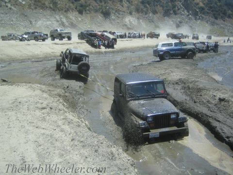 1987 Suzuki Samurai - Multiple off-road vehicles navigate a muddy terrain, with one Jeep Wrangler struggling in the mire.