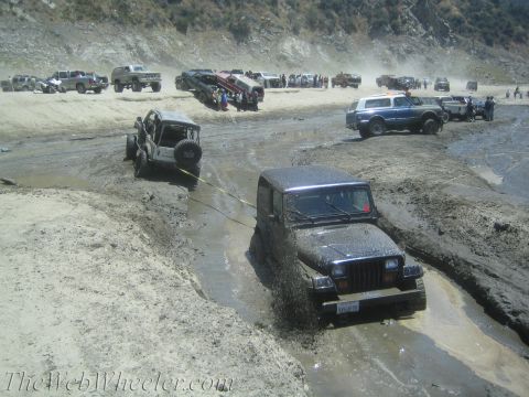 1987 Suzuki Samurai - Multiple off-road vehicles navigate a muddy terrain, with one Jeep appearing stuck and being assisted by another.