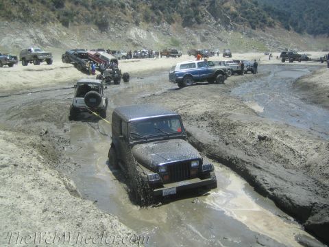 1987 Suzuki Samurai - Multiple Jeeps navigating a muddy off-road course with one vehicle stuck.