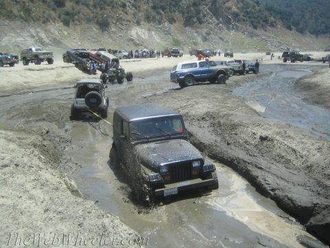 1987 Suzuki Samurai - Multiple off-road vehicles navigate a muddy terrain, with one Jeep being towed out of a deep mud pit.