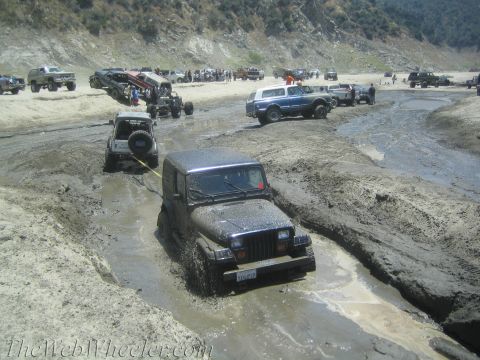 1987 Suzuki Samurai - Multiple off-road vehicles navigate a muddy terrain, with one Jeep Wrangler requiring a tow.
