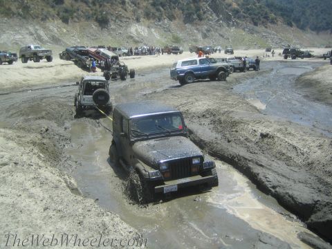 1987 Suzuki Samurai - A Jeep Wrangler is being pulled out of a muddy trench by another vehicle during an off-road event.