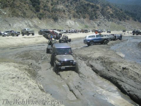 1987 Suzuki Samurai - Multiple off-road vehicles navigate a muddy terrain under a bright sky.