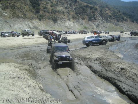 1987 Suzuki Samurai - Multiple off-road vehicles navigate a challenging muddy terrain during an event.