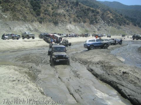 1987 Suzuki Samurai - A group of off-road vehicles navigate a challenging muddy terrain, with several vehicles bogged down.