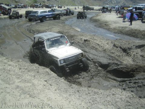1987 Suzuki Samurai - A Suzuki Samurai navigates a muddy track, surrounded by other off-road vehicles and spectators.