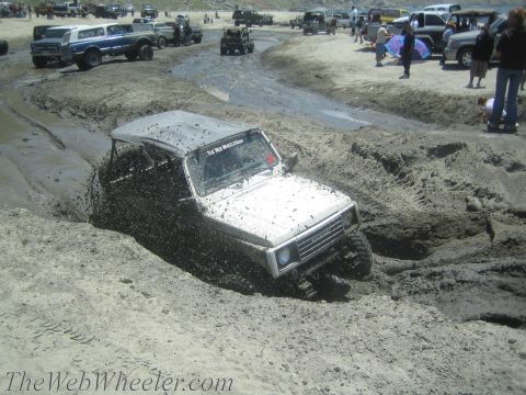 1987 Suzuki Samurai - Off-road vehicle navigating a challenging mud pit, with several other trucks and people visible.