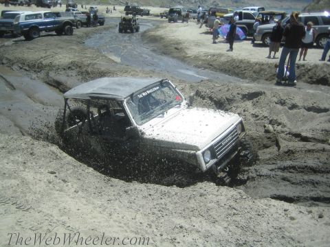 1987 Suzuki Samurai - A white 1987 Suzuki Samurai navigates a muddy off-road course with other vehicles in the background.