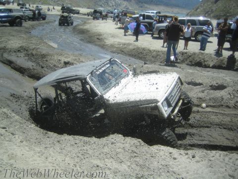 1987 Suzuki Samurai - A white 1987 Suzuki Samurai navigates a muddy off-road course, kicking up dirt and water.