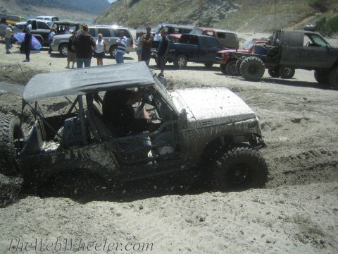 1987 Suzuki Samurai - A Suzuki Samurai is stuck in the mud at a sandy off-road event with other vehicles and spectators present.