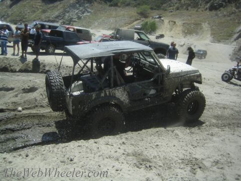 1987 Suzuki Samurai - This Suzuki Samurai is shown off-roading through mud and dirt, with other vehicles visible in the background.