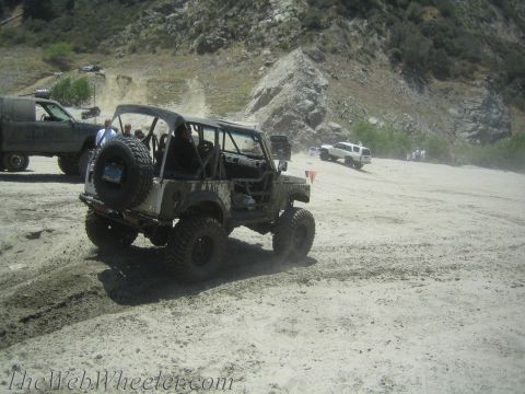 1987 Suzuki Samurai - Several vehicles are navigating a dusty, off-road trail with steep, rocky hillsides.