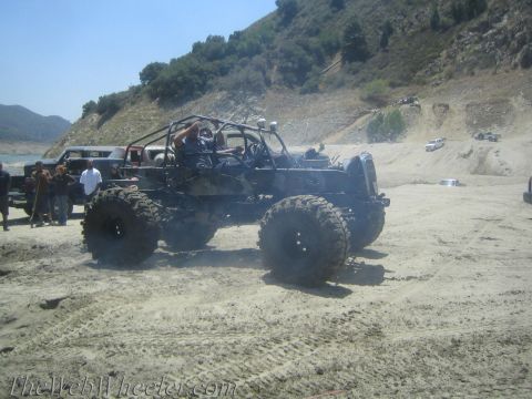 1987 Suzuki Samurai - A heavily modified off-road buggy with oversized tires and a custom roll cage is seen in a sandy, outdoor environment.