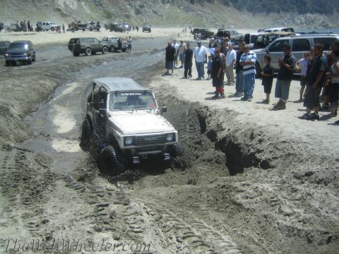1987 Suzuki Samurai - Suzuki Samurai tackles a challenging muddy obstacle on the beach, drawing a crowd.
