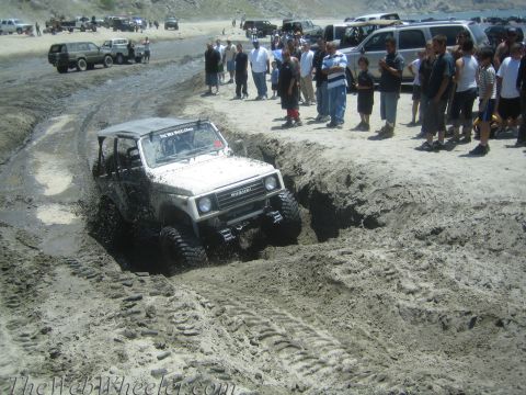 1987 Suzuki Samurai - A 1987 Suzuki Samurai navigates a challenging muddy terrain, kicking up water and dirt.