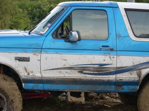 1992 Ford Bronco - Muddy blue and white 1992 Ford Bronco side view with a prominent Bronco badge.