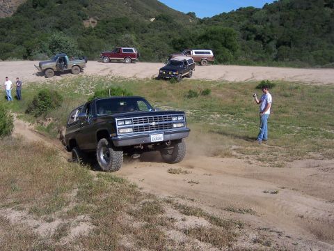 1991 Ford Bronco - Several SUVs are seen off-roading on a sunny day in a hilly, grassy area.