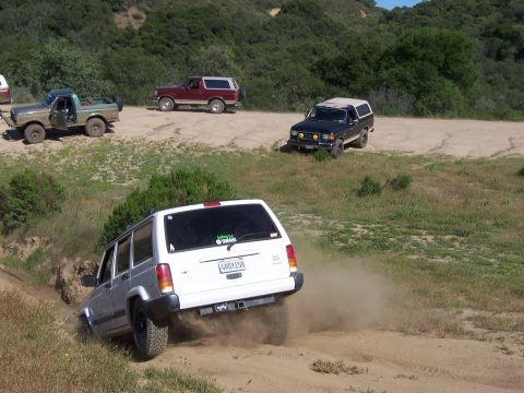 1991 Ford Bronco - Multiple Ford Broncos and a Jeep Cherokee navigate a dusty trail during an off-road event.