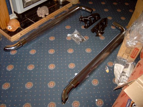 1989 Ford Bronco - Uninstalled exhaust pipes and manifolds are laid out on a patterned carpet next to boxes.
