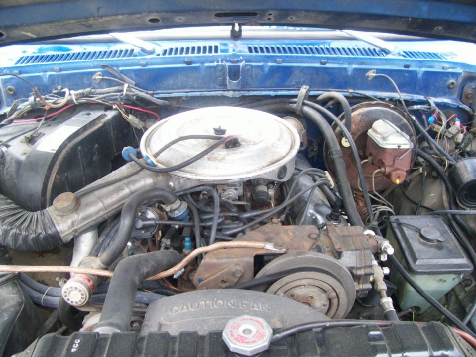 Engine bay with round air cleaner, CAUTION FAN shroud, brake booster, and wiring in a blue vehicle