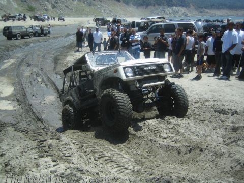 1987 Suzuki Samurai - Suzuki Samurai tackles muddy terrain with spectators observing the off-road action.