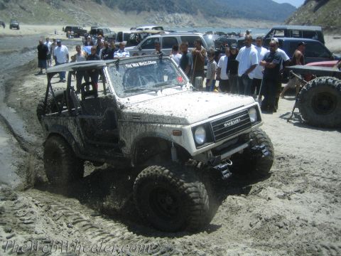 1987 Suzuki Samurai - A white 1987 Suzuki Samurai navigates a muddy, sandy terrain with onlookers in the background.