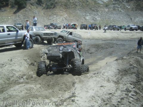 1987 Suzuki Samurai - Multiple off-road vehicles are seen navigating a muddy terrain with spectators observing the action.
