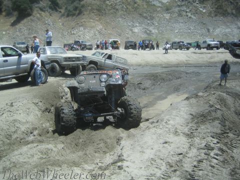 1987 Suzuki Samurai - A heavily modified Jeep tackles a challenging sandy terrain with other vehicles and spectators in the background.