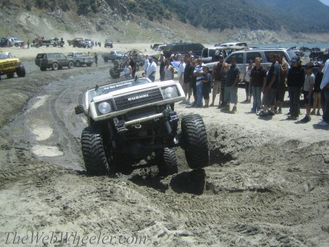 1987 Suzuki Samurai - A modified 1987 Suzuki Samurai tackles a challenging muddy terrain, drawing a crowd of onlookers.