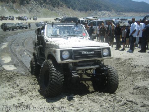 1987 Suzuki Samurai - A white Suzuki Samurai navigates a muddy, sandy terrain with other vehicles and people in the background.
