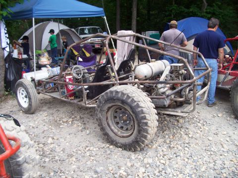 1989 Ford Bronco II - A custom-built buggy with a roll cage and large tires sits on a gravel surface, with tents and people in the background.