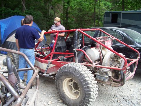 1989 Ford Bronco II - A red dune buggy with a prominent roll cage and off-road tires is seen parked outdoors, with people and other vehicles nearby.