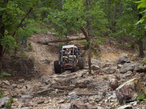 1989 Ford Bronco II - An off-road buggy navigates a challenging rocky terrain surrounded by trees.