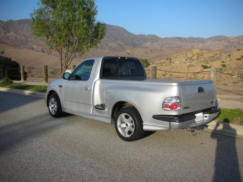 1998 Ford Crown Victoria - This silver pickup truck is parked on a road with a scenic mountain backdrop.