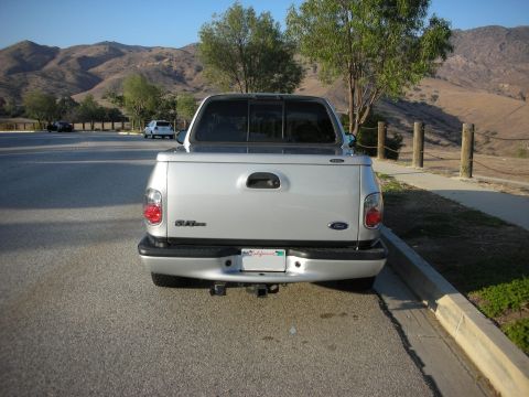 1998 Ford Crown Victoria - Rear view of a silver 1998 Ford F-150 pickup truck parked on the side of a road with a mountainous landscape in the background.