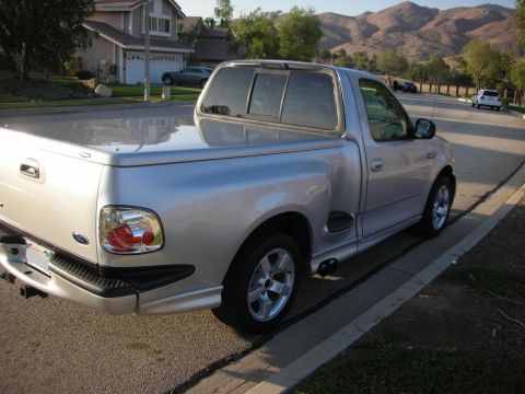 1998 Ford Crown Victoria - This silver Ford F-150 SVT Lightning pickup truck is parked on a street with mountains in the background.