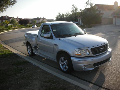 1998 Ford Crown Victoria - A silver Ford F-150 SVT Lightning is parked curbside on a sunny day in a residential area.