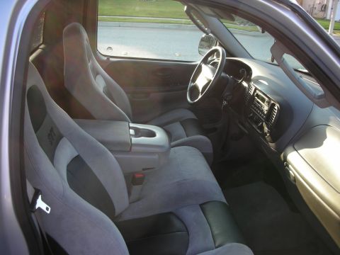 1998 Ford Crown Victoria - Interior shot through the open passenger door of a Ford truck cab with gray two-tone SVT-embroidered sport bucket seats, a flip-down center…