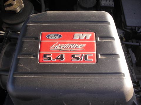 1998 Ford Crown Victoria - Close-up of a black plastic engine/air box cover in an engine bay wearing the red Ford SVT Lightning 5.4 S/C badge plate. Surrounding hoses…