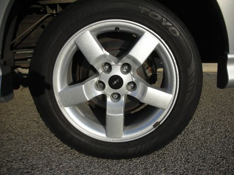 1998 Ford Crown Victoria - Close-up of a silver five-spoke SVT-center-cap alloy wheel with a Toyo Proxes tire on a silver truck, shot at the rear wheel over asphalt.…